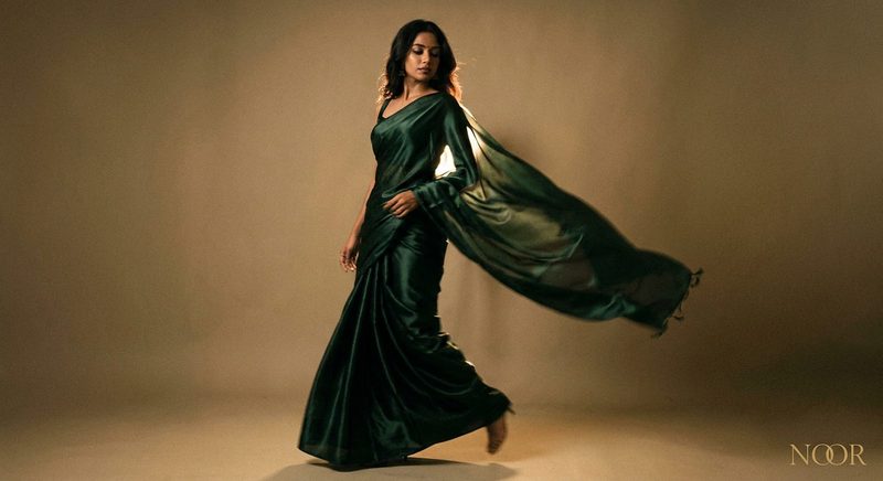 Woman in a flowing emerald satin saree mid-turn in a warm studio