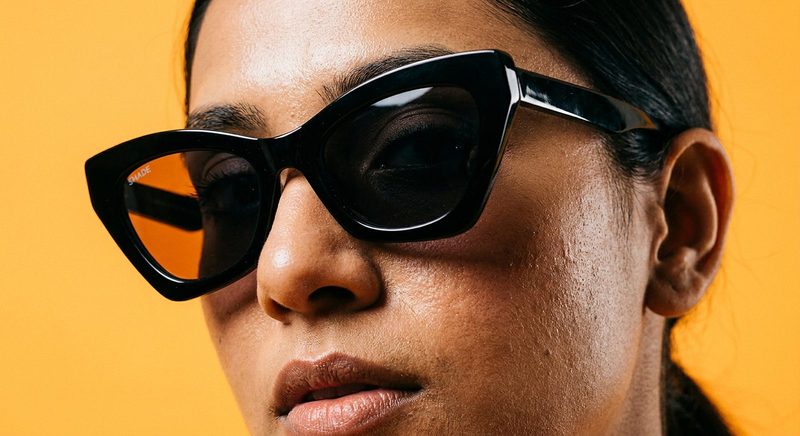 Close-up of a woman in black cat-eye sunglasses on an orange backdrop