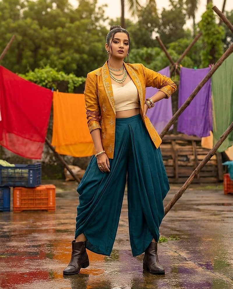 Woman in a mustard jacket and teal dhoti trousers among colourful drying fabrics