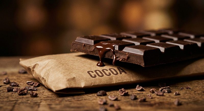 Dark chocolate bar with a melted drizzle on a kraft cocoa pouch with cacao nibs