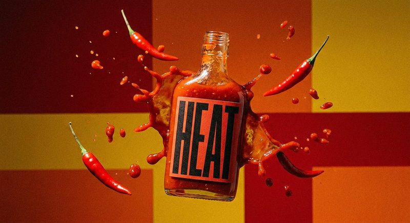 Hot sauce bottle bursting with red chillies and sauce on a red and yellow backdrop