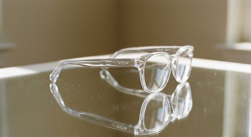 Clear-frame eyeglasses on a reflective glass surface in sunlight