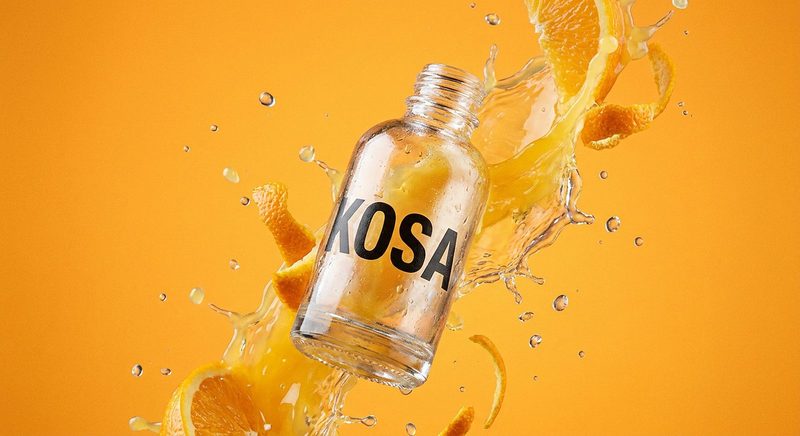 Clear serum bottle caught mid-splash with orange slices on a saffron backdrop