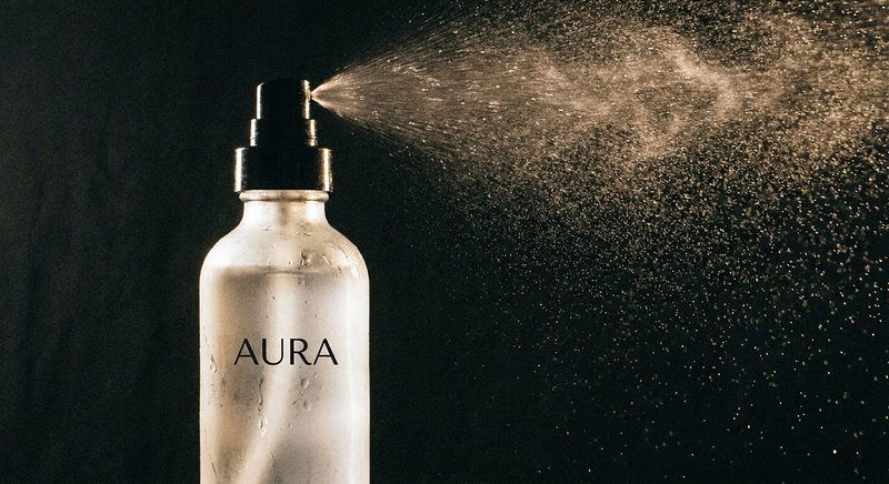 Fine mist spraying from a clear glass bottle against a dark background