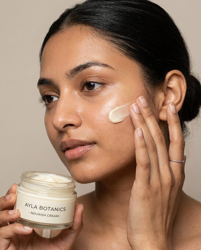 Woman applying cream to her cheek while holding an open jar
