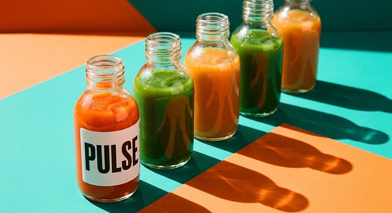 Row of cold-pressed juice bottles in orange and green on a colour-block backdrop